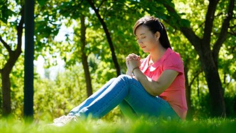 一個年輕姊妹坐在草地上禱告